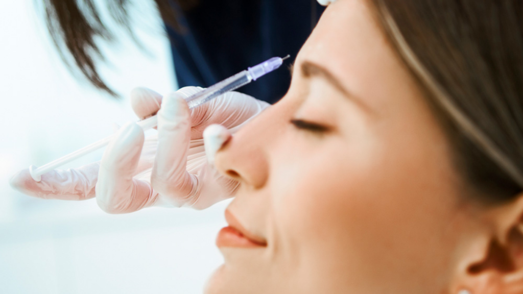 A gloved medical injector administers a Botox® injection to a woman's forehead between her brows during a treatment.